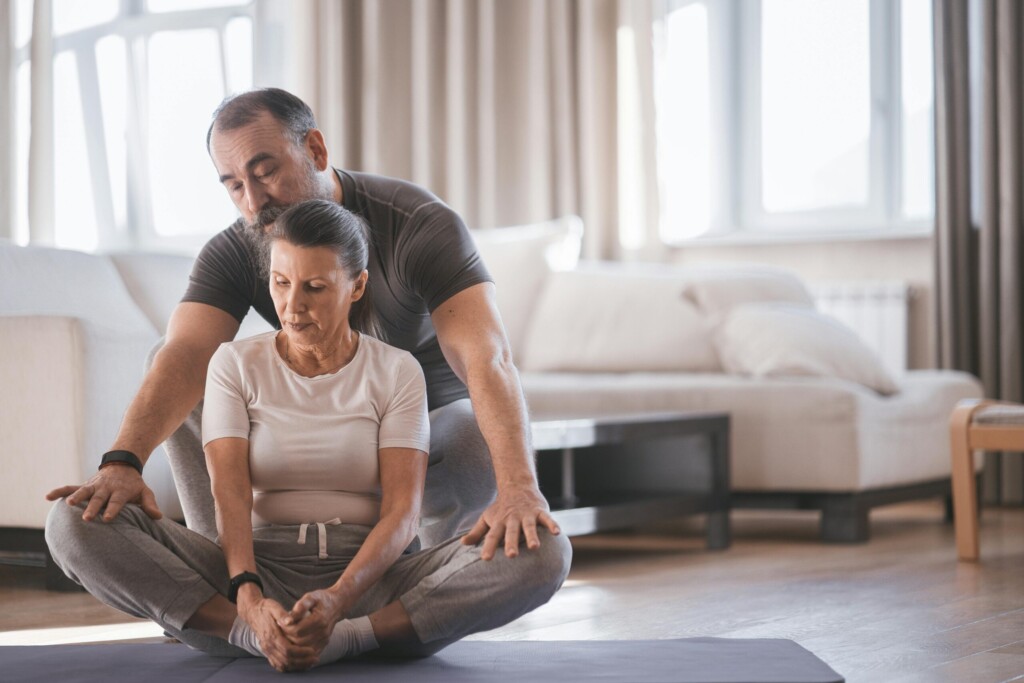a senior couples practice butterfly yoga pose in home