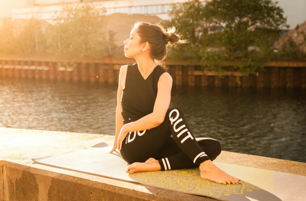 Yoga practitioner performing Ardha-Matsyendrasana (Half Lord of the Fishes Pose), sitting on the mat with one leg crossed over the other, and twisting the torso to bring the opposite elbow to the outer knee. The pose stretches the spine, hips, and shoulders, while improving flexibility and aiding digestion.
